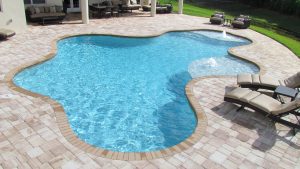 Curved swimming pool south Florida in backyard, with tile flooring and deck chairs