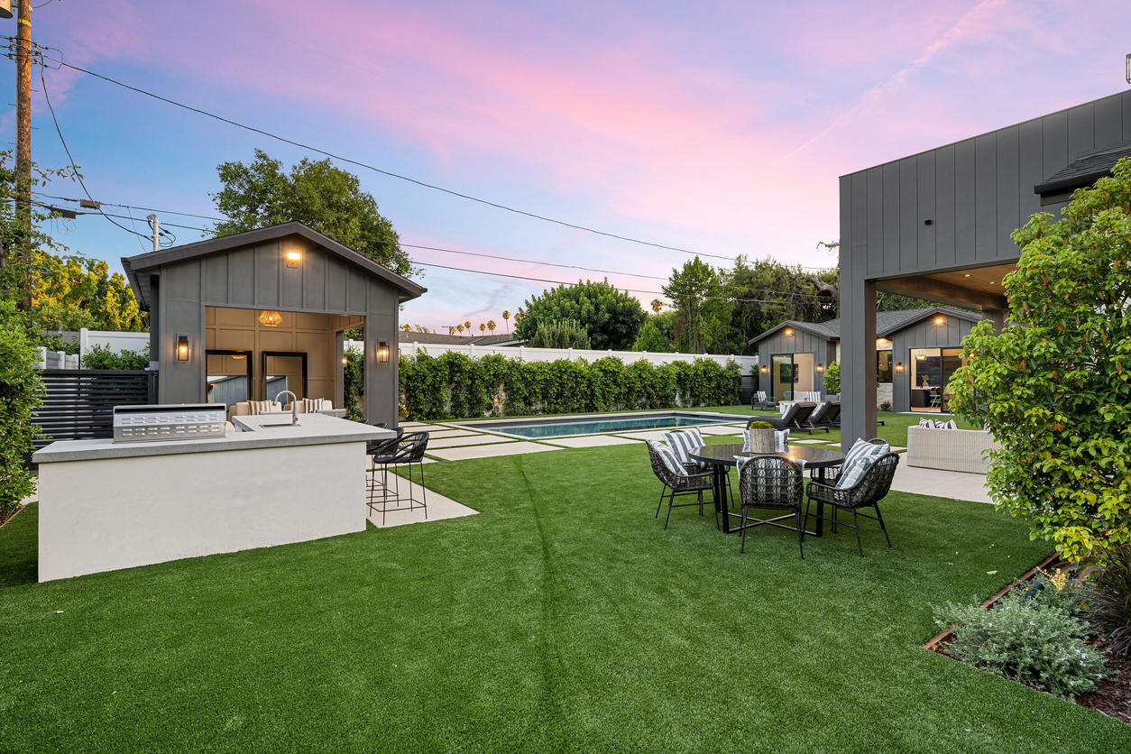 Luxury backyard with pool, outdoor kitchen, and seating area at sunset.