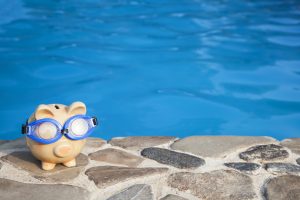 Summer piggy bank wearing swimming goggles in front of a pool