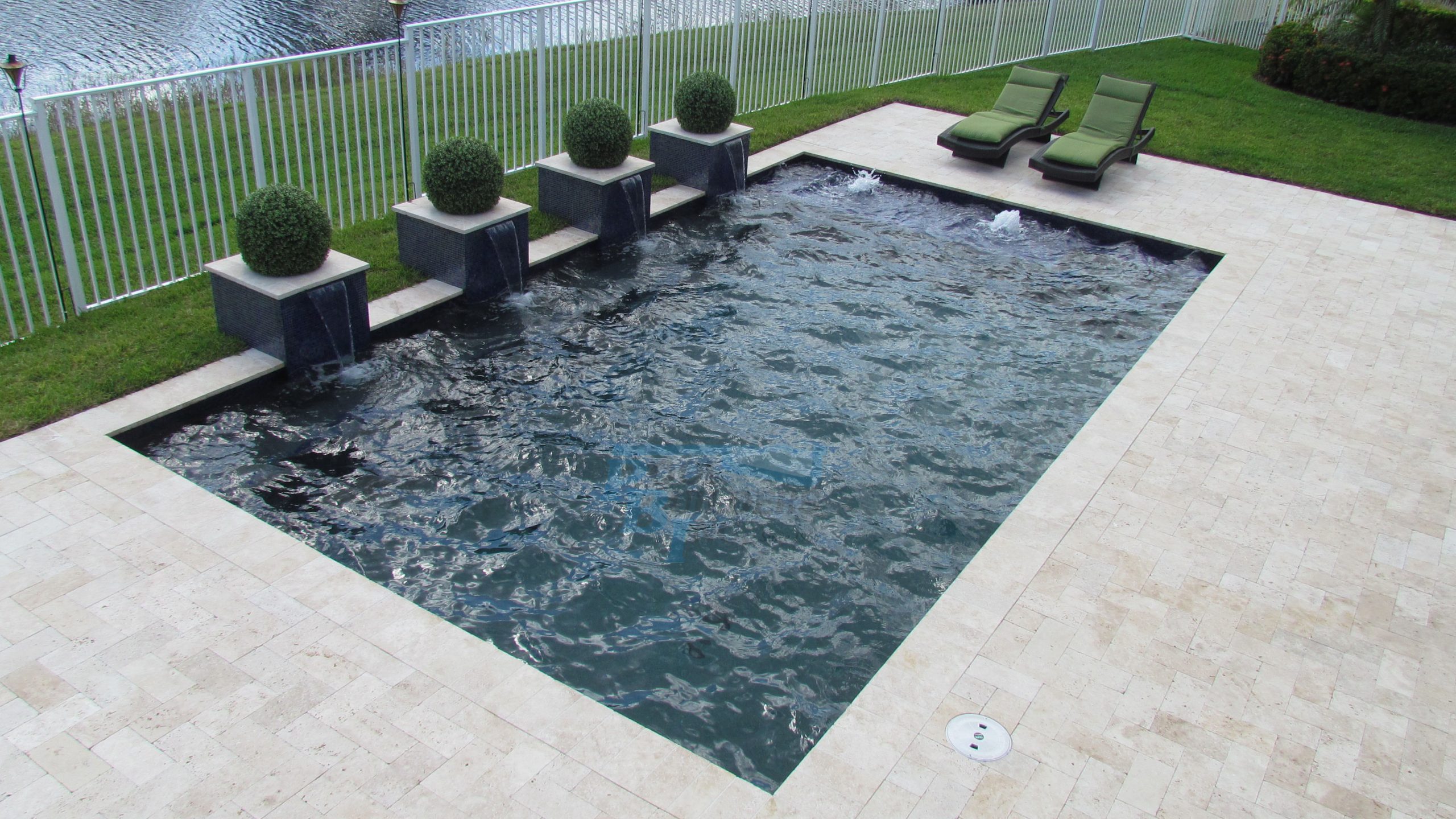 Geometric swimming pool design with modern water features and potted greenery by Pool Builders Inc. in South Florida